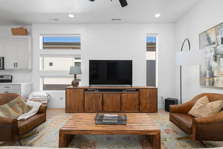 Recessed lighting, wood-finish flooring, white cabinetry with dark hardware, natural wood media console, and a contemporary ceiling fan