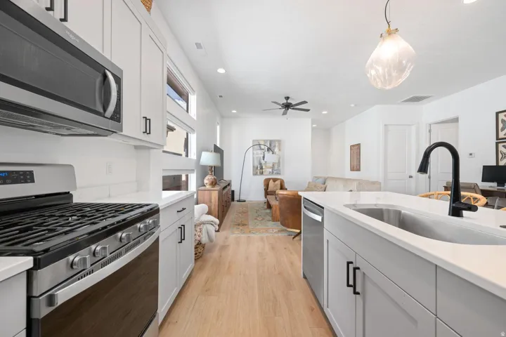 Modern kitchen featuring stainless steel appliances, light wood-finish flooring, white cabinetry with black hardware, and an island with an undermount sink and matte black faucet