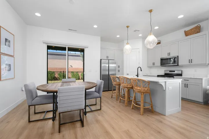 Light wood-finish flooring throughout, a large kitchen island with a stone-finish countertop, light gray cabinetry, and stainless steel appliances