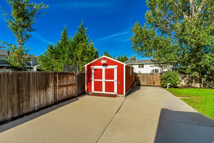 Red-painted storage shed with white trim, double doors, concrete slab, and wood privacy fencing