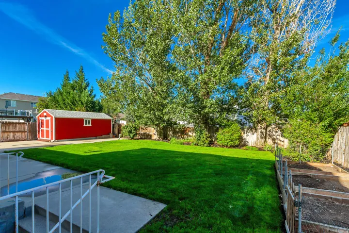 Expansive green lawn, mature trees, concrete patio, red storage shed, and wood fencing