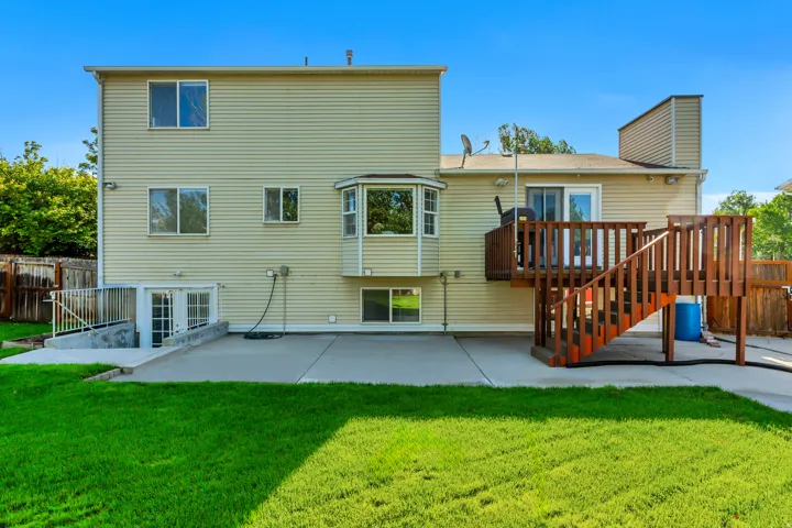 Expansive backyard featuring a manicured lawn, a concrete patio, a wooden deck with stairs, a bay window, and a walk-out basement entry with double doors