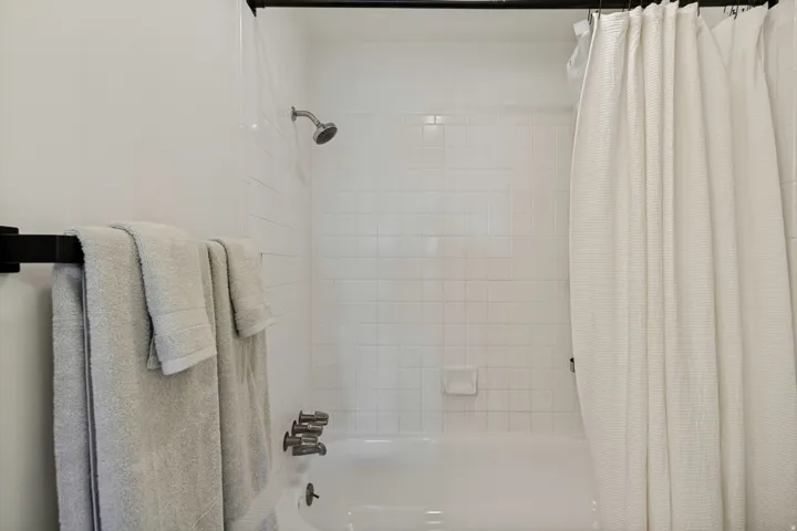 Bathtub with white subway tile surround, chrome shower fixtures, and a black towel bar