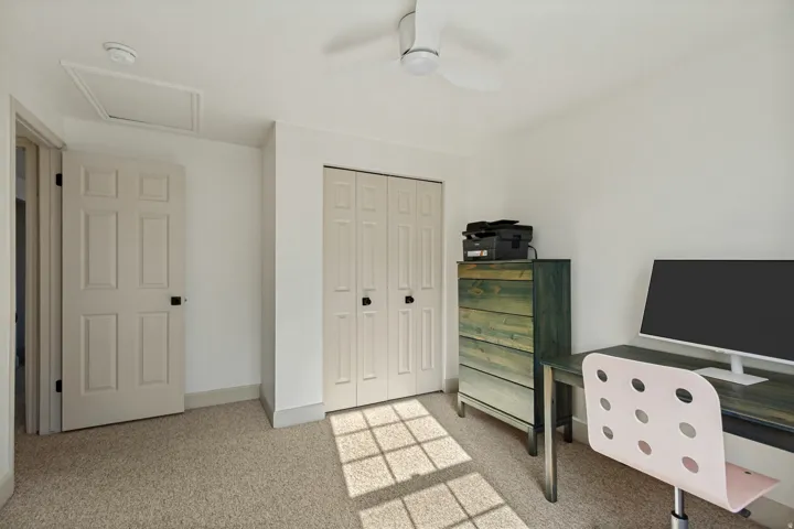 Light-colored carpeted flooring, white walls, a six-panel interior door, bi-fold closet doors, and a ceiling fan