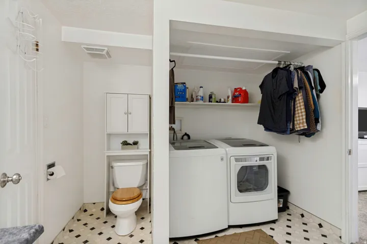 White washer and dryer units, built-in shelving, white over-the-toilet cabinet, wood-finish toilet seat, and patterned flooring