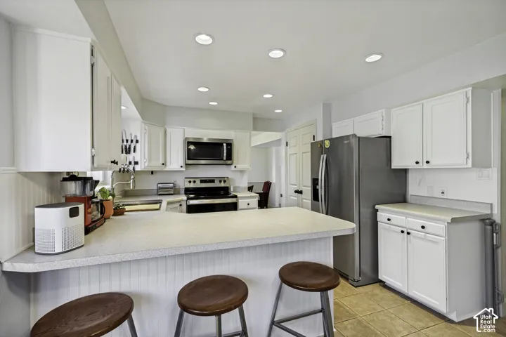 Kitchen featuring white cabinetry, stainless steel appliances, recessed lighting, a breakfast bar, and tile flooring