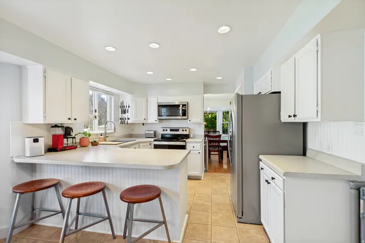 White cabinetry, stainless steel appliances, recessed lighting, tile flooring, and a breakfast bar
