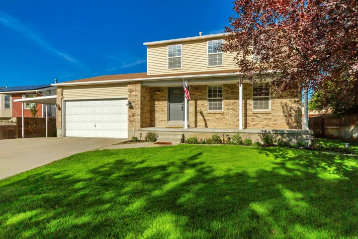 Two-story residence featuring a brick facade, covered front porch, integrated garage, and a manicured lawn