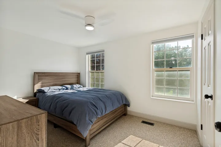 White walls, two windows, textured carpeting, and a ceiling fan with integrated lighting