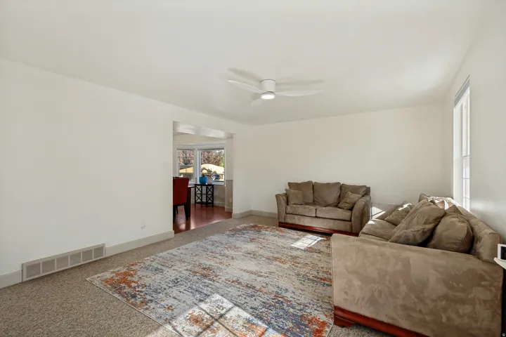 Carpeted living space with a ceiling fan, recessed doorway, and a window providing natural light
