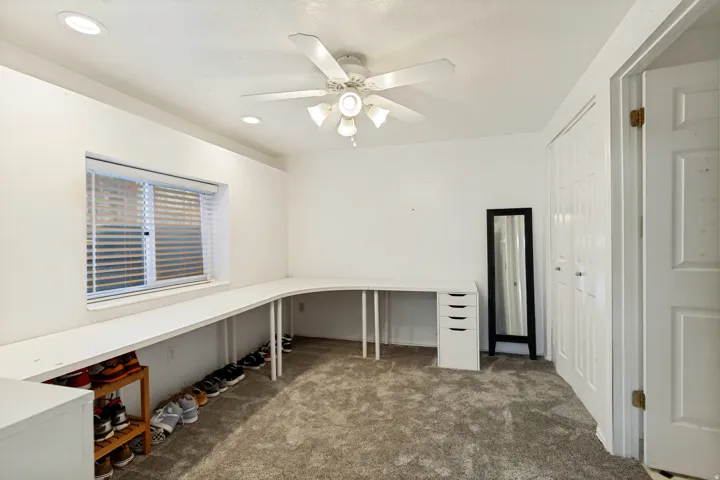 White built-in desk, window with blinds, ceiling fan with light, recessed lighting, and carpeted flooring