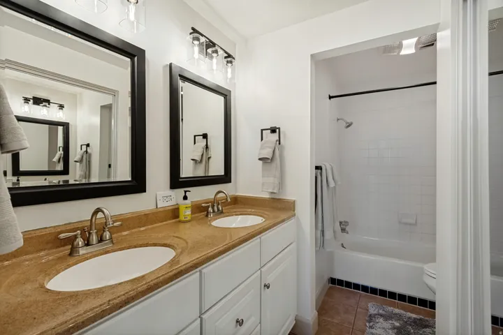Double vanity with integrated sinks and brushed nickel faucets, dark framed mirrors, white shaker-style cabinetry, and a shower-over-tub combination with white subway tile surround