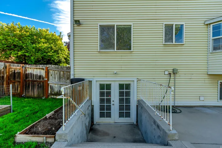 Walk-out basement access with white French doors, concrete patio, and fenced yard