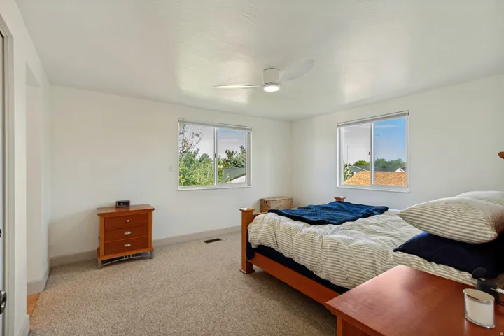 Light-toned carpet flooring, two windows with white frames, a white ceiling fan with integrated lighting, and white wall finishes