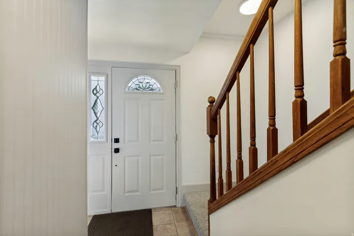 Entry door with an arched decorative glass insert and sidelight, complemented by a wood-finish staircase railing and balusters