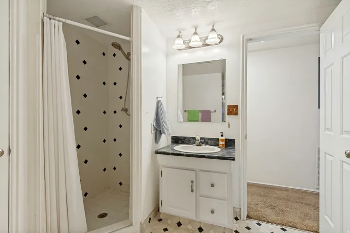 Walk-in shower with decorative wall accents, single vanity with dark countertop, white cabinetry with silver hardware, and a framed mirror