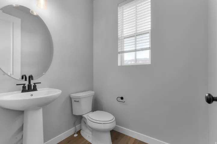 Pedestal sink with a matte black faucet, oval mirror, and wood-finish flooring