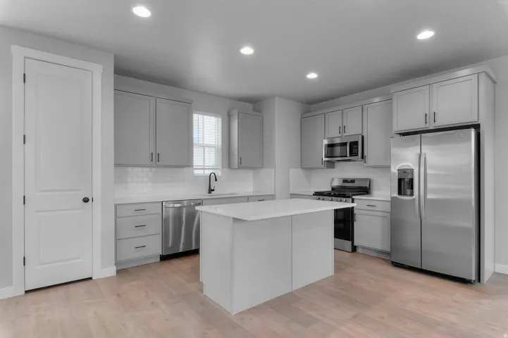 Kitchen with wood-finish flooring, recessed lighting, a central island, stainless steel appliances, and gray cabinetry