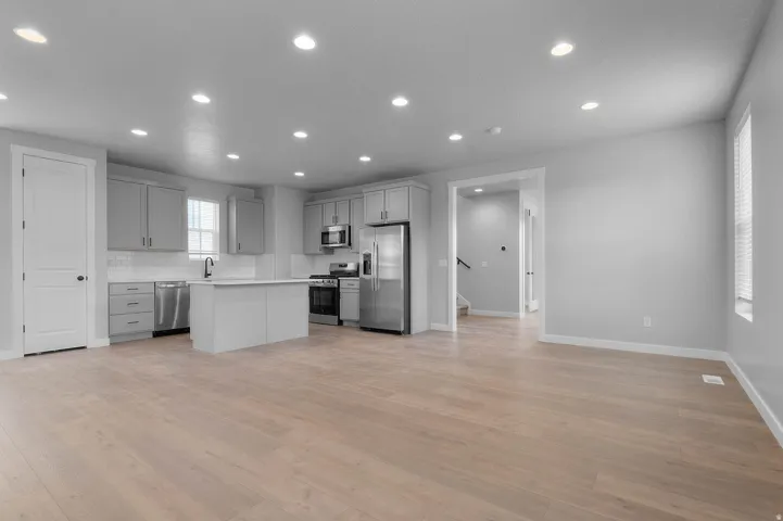 Open-concept living area featuring wood-finish flooring, recessed lighting, and a kitchen with gray cabinetry, white subway tile backsplash, and stainless steel appliances