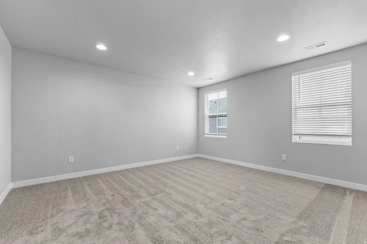 Recessed lighting, light gray wall finishes, two windows with blinds, and neutral tone carpeting