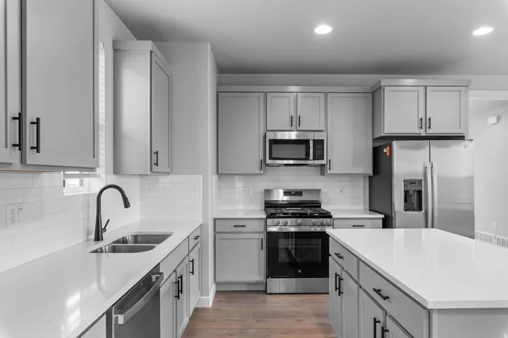 Kitchen featuring light gray cabinetry, white countertops, stainless steel appliances, a subway tile backsplash, and wood-finish flooring