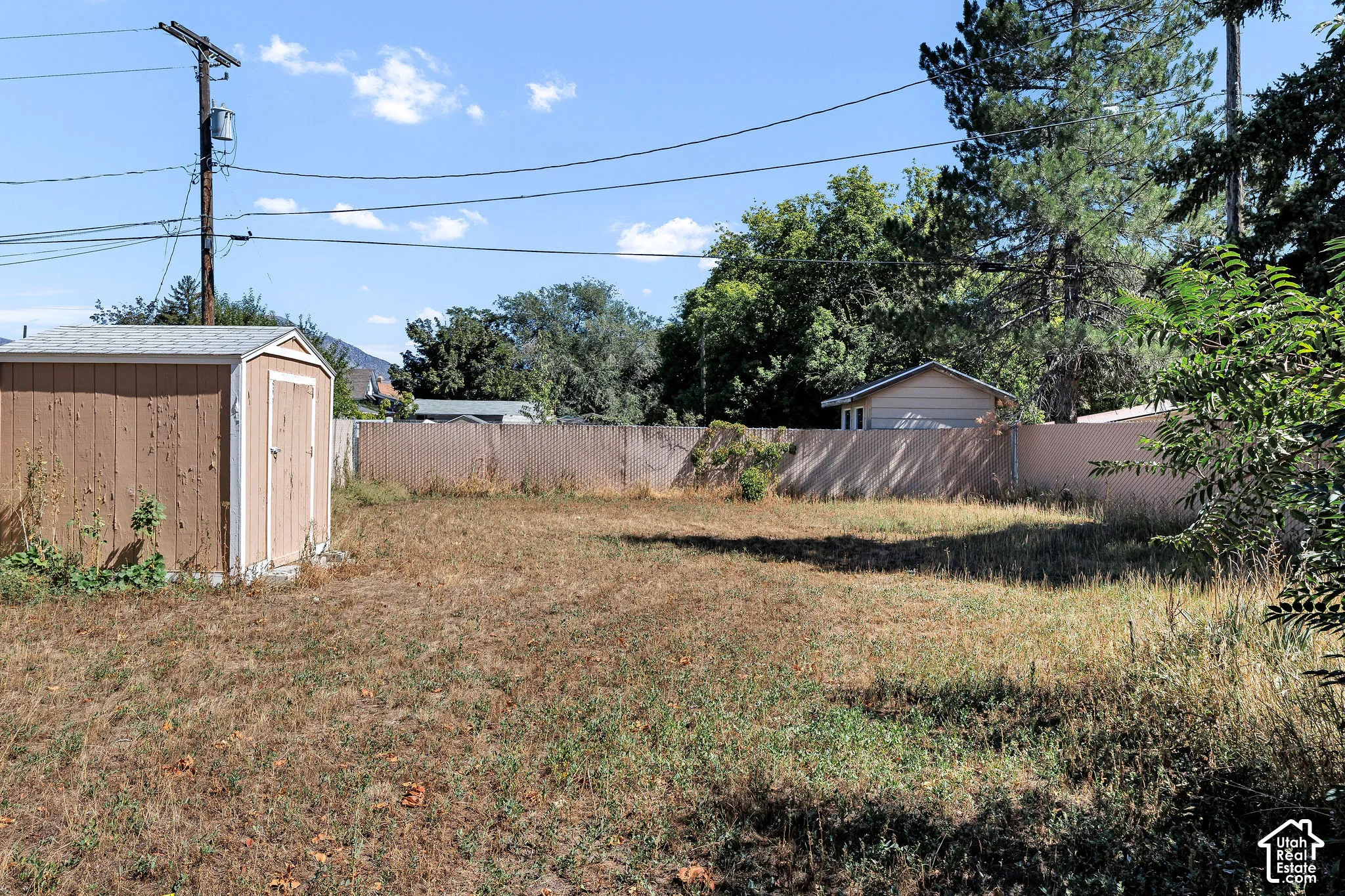 Expansive yard featuring a wood-sided storage shed, wood fencing, and mature perimeter trees