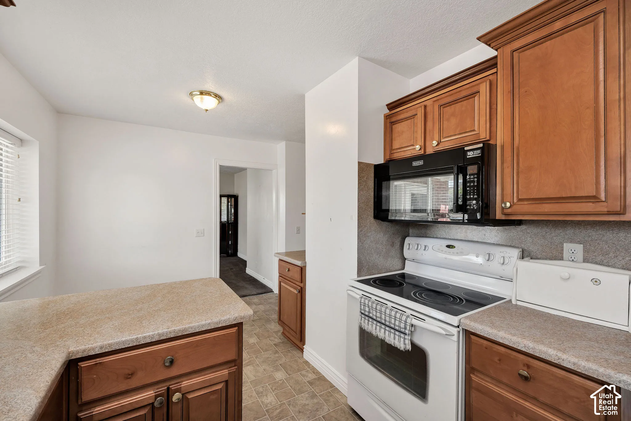 Kitchen with wood-finish cabinetry, solid surface countertops, a built-in microwave, an electric range, and tile flooring