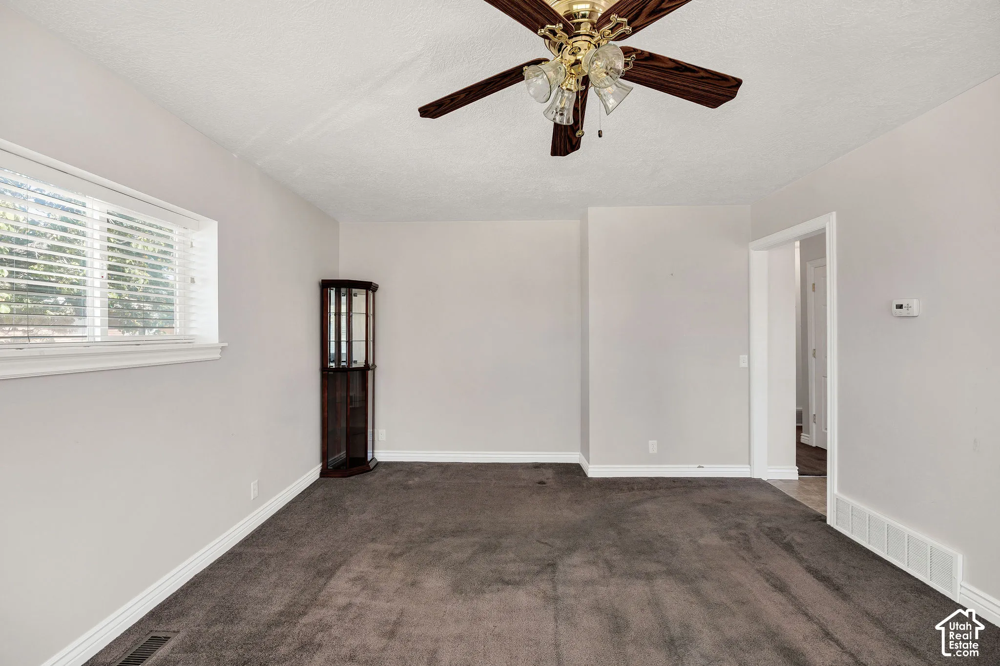 Recessed window with horizontal blinds, overhead ceiling fan with lighting, and doorway with white trim