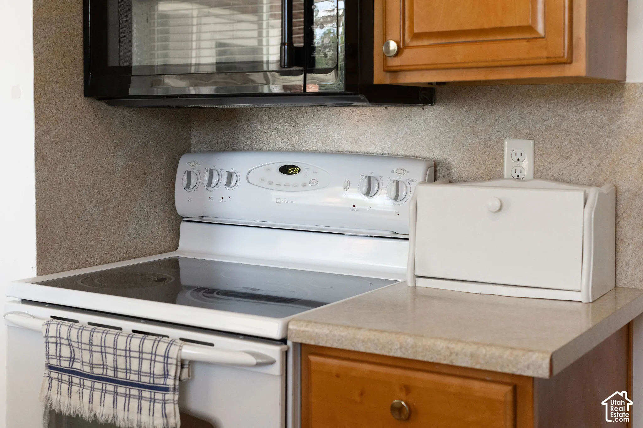 White electric range with a black cooktop, complemented by an overhead microwave and wood-finish cabinetry