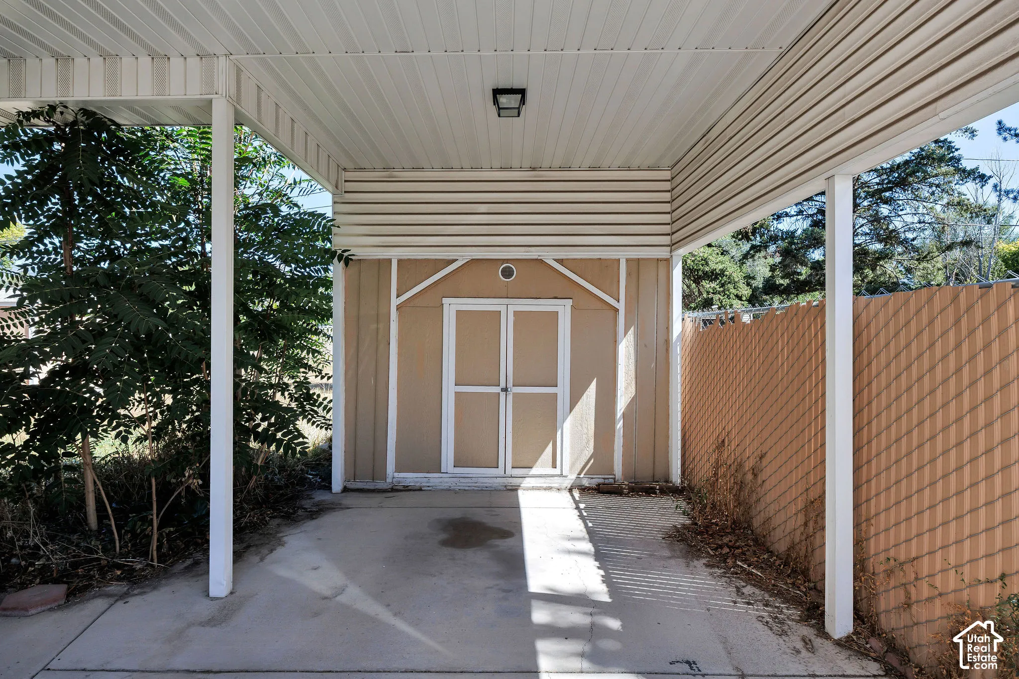 Covered carport featuring a flush-mount overhead light, concrete flooring, and a storage shed with double doors