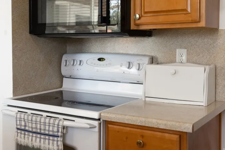 White electric range with a black cooktop, complemented by an overhead microwave and wood-finish cabinetry