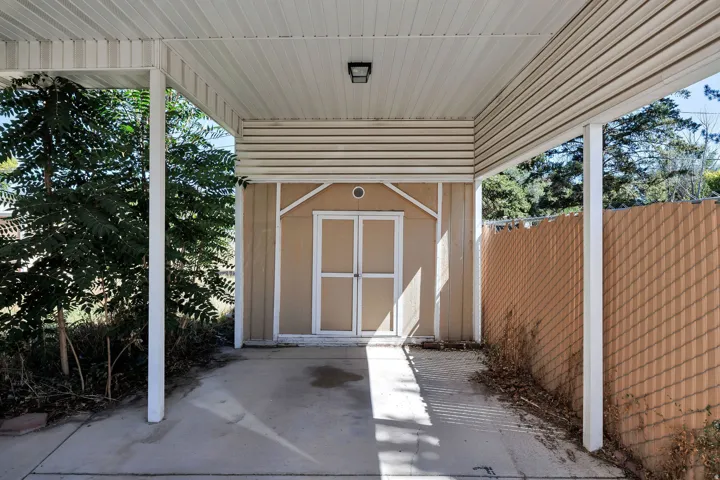Covered carport featuring a flush-mount overhead light, concrete flooring, and a storage shed with double doors