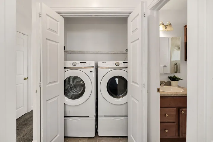 Laundry closet featuring a front-loading washer and dryer, elevated on pedestals, with wire shelving