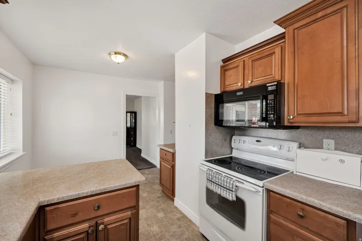 Kitchen with wood-finish cabinetry, solid surface countertops, a built-in microwave, an electric range, and tile flooring