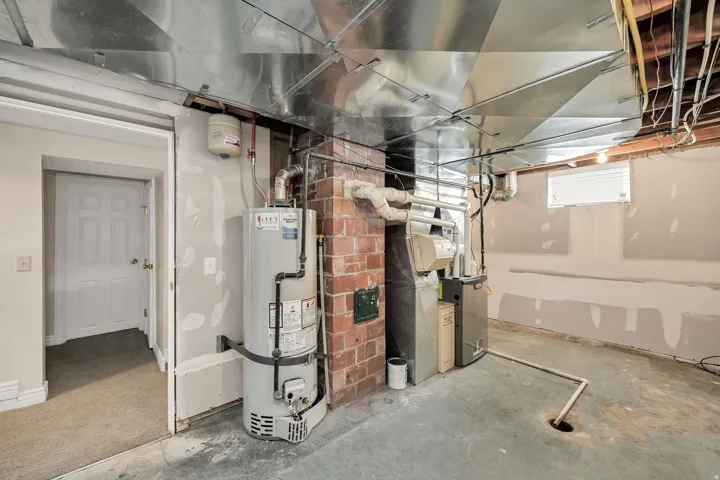 Exposed ductwork, brick chimney, water heater, and furnace in a utility space