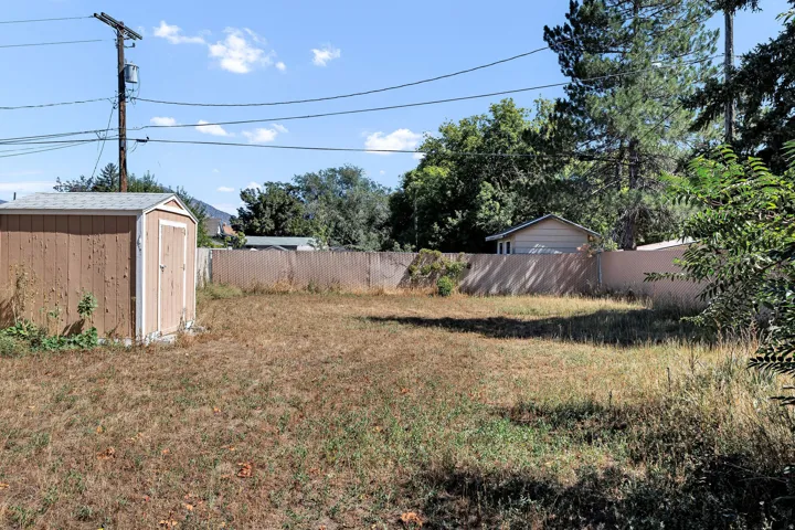 Expansive yard featuring a wood-sided storage shed, wood fencing, and mature perimeter trees