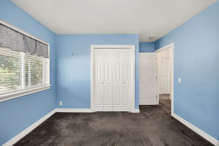Carpeted room featuring a white-framed window with blinds, bi-fold closet doors, and light blue wall finishes