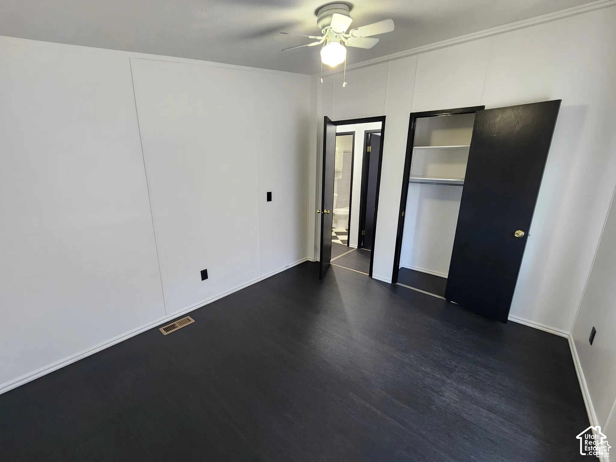 Room featuring dark wood-finish flooring, white panel walls, and a ceiling fan