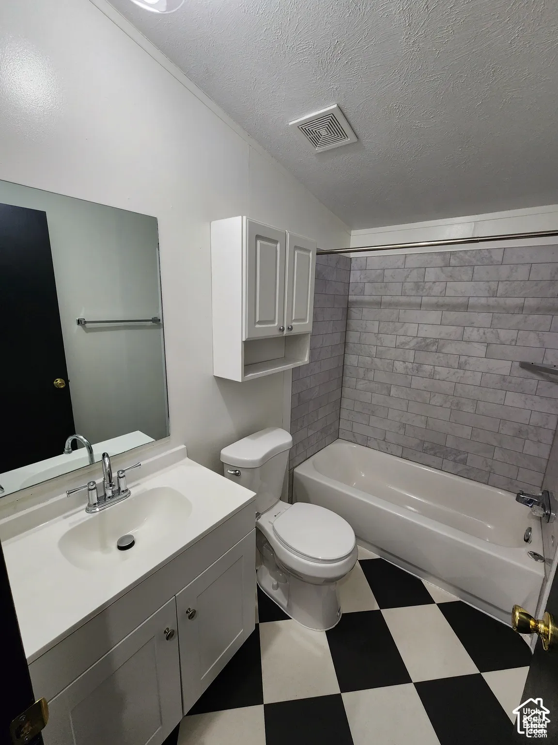 Bathroom featuring a white vanity with integrated sink, chrome faucet, wall-mounted mirror, white wall cabinetry, and a white bathtub with subway tile surround