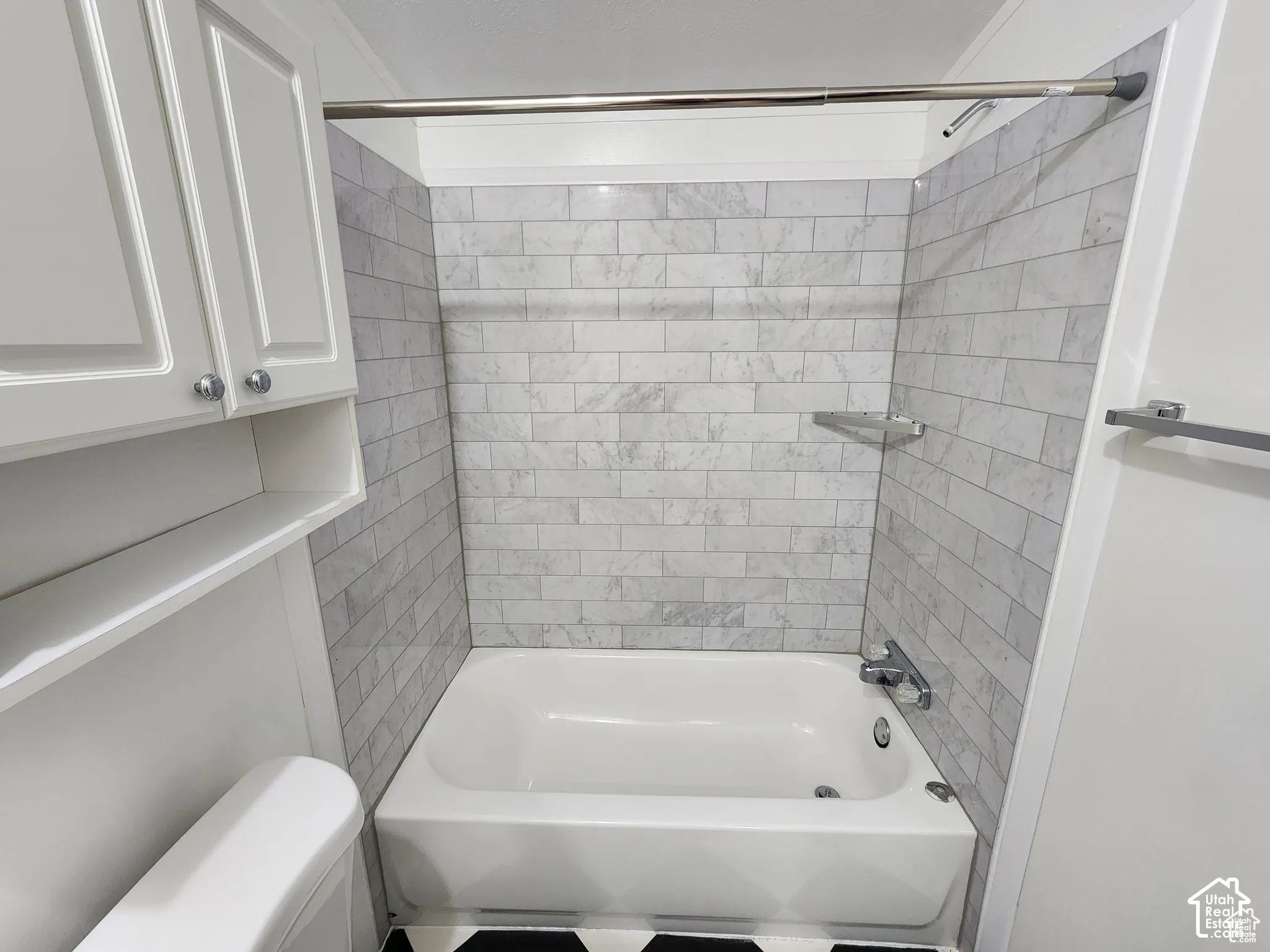 White bathtub with subway-style tiled surround, chrome fixtures, and corner shelving