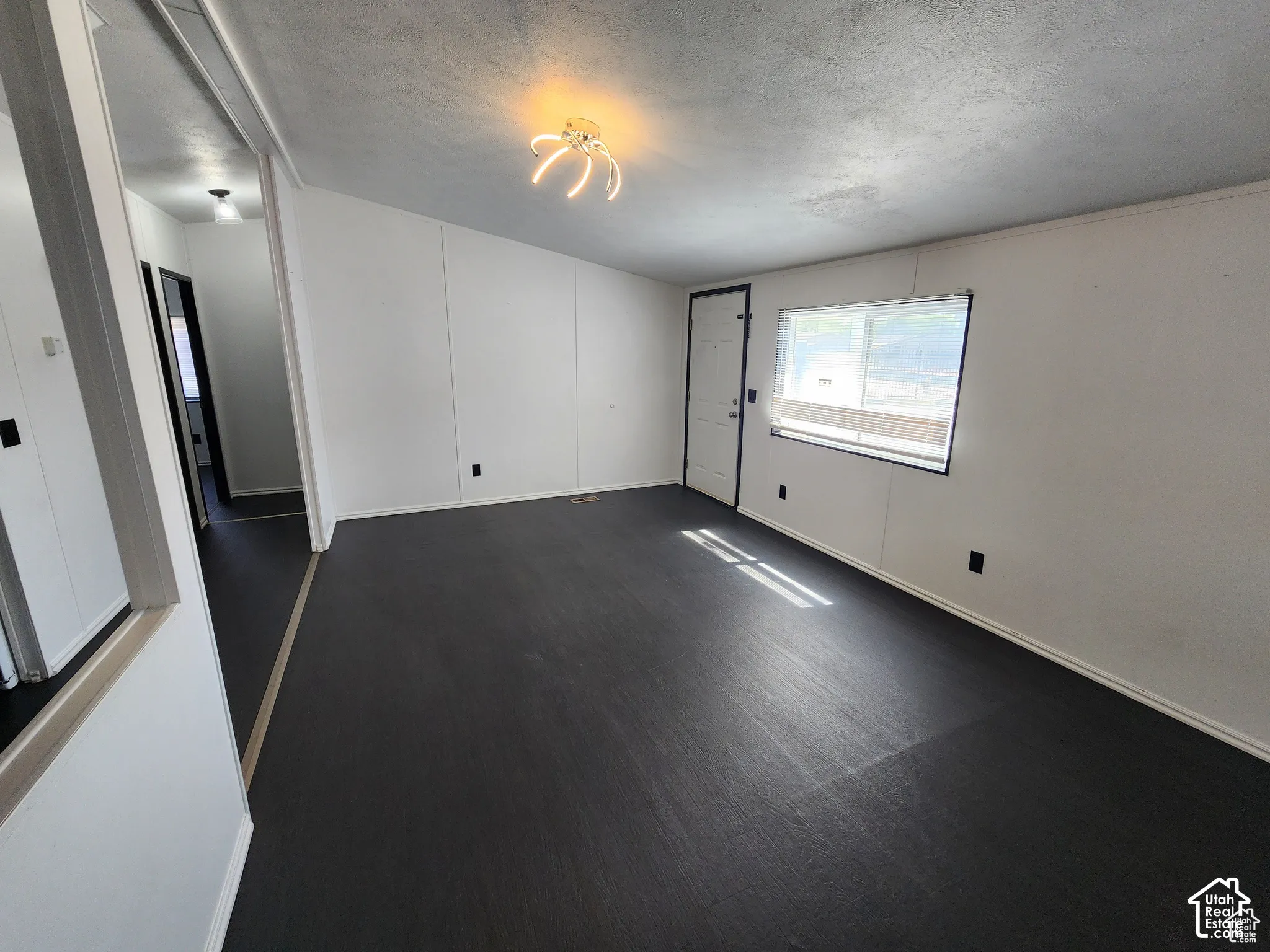 Spacious living area with dark flooring, white panel walls, and an overhead lighting fixture