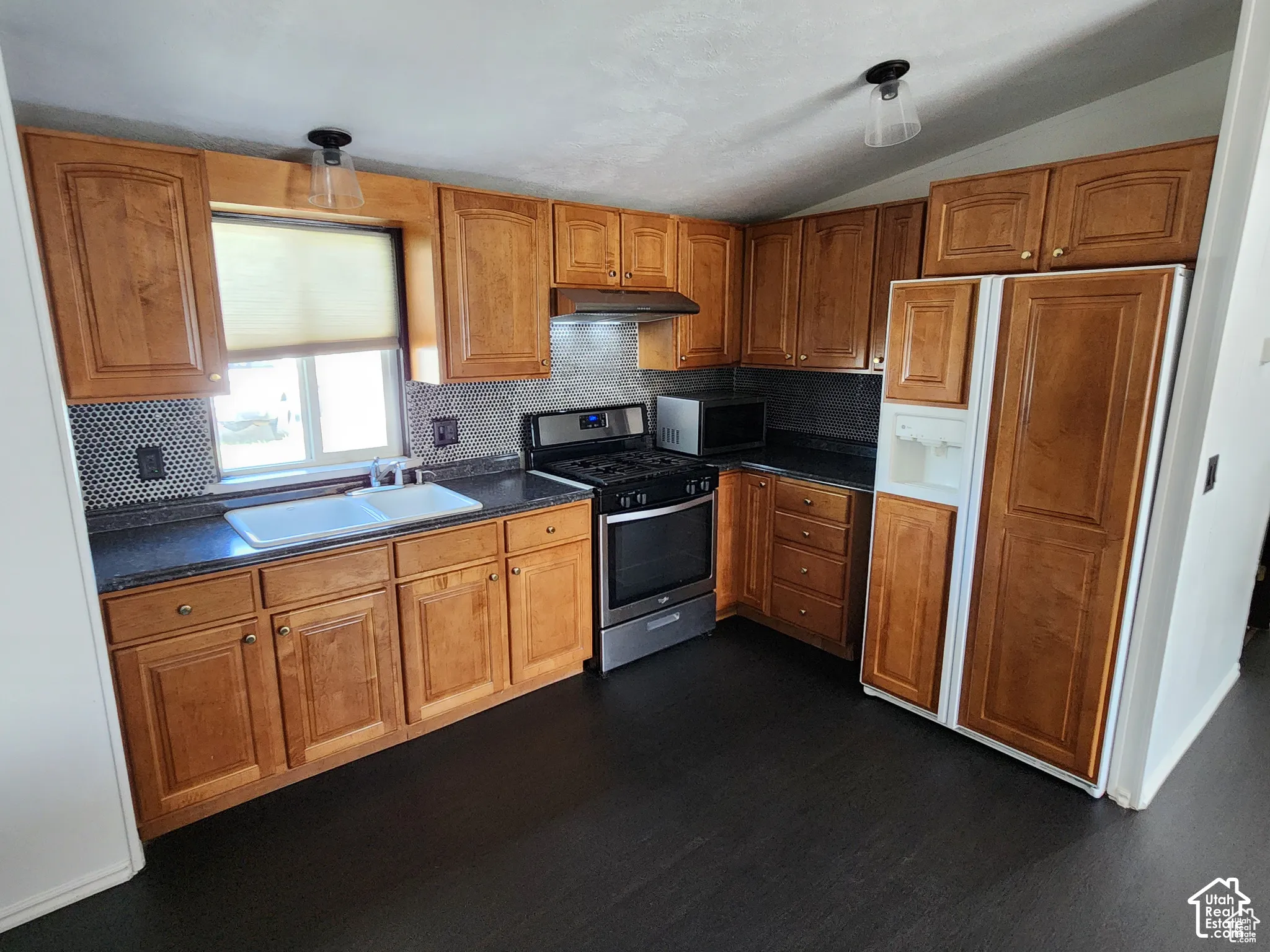 Kitchen featuring wood-finish cabinetry, dark countertops, a stainless steel range, and a dual basin sink