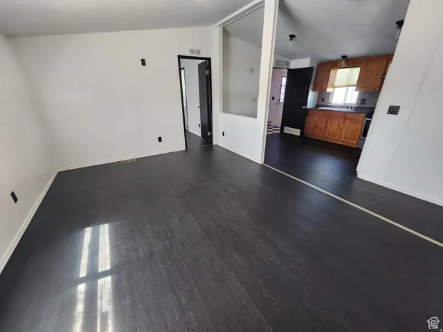 Dark wood-finish flooring, white walls, and a partial wall with an open concept to the kitchen