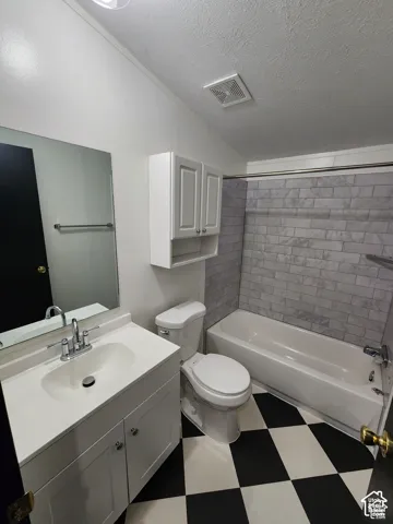 Bathroom featuring a white vanity with integrated sink, chrome faucet, wall-mounted mirror, white wall cabinetry, and a white bathtub with subway tile surround