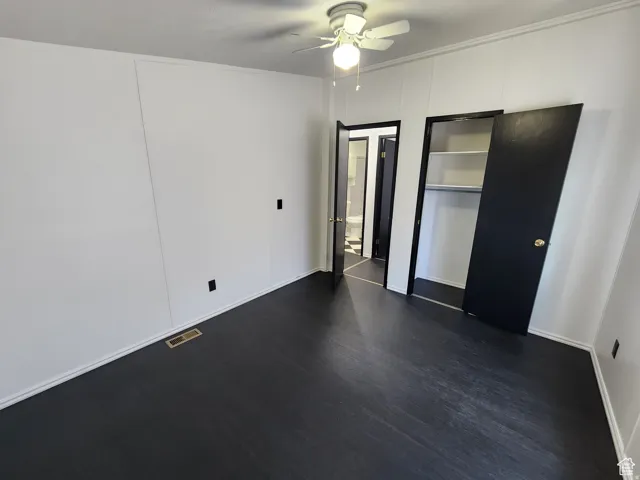 Room featuring dark wood-finish flooring, white panel walls, and a ceiling fan