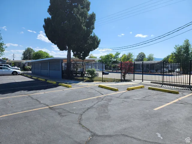 Paved parking area with yellow parking blocks, featuring a black wrought iron fence and mature trees