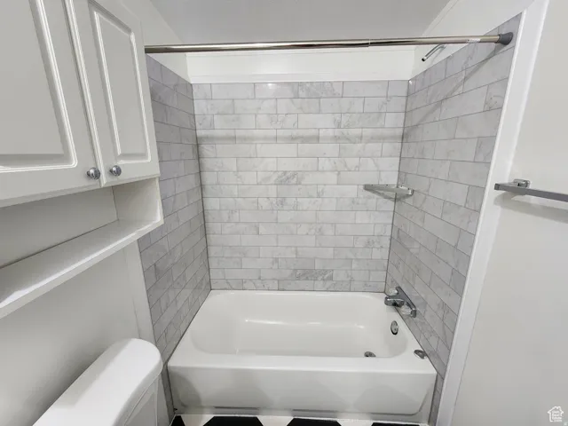 White bathtub with subway-style tiled surround, chrome fixtures, and corner shelving