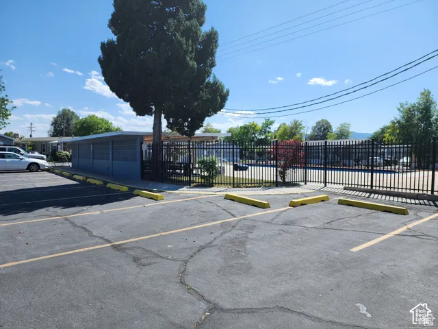 Paved parking area with yellow parking blocks, featuring a black wrought iron fence and mature trees