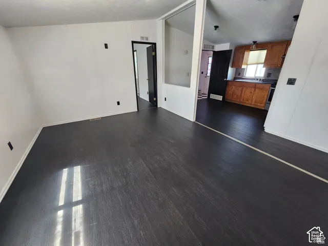 Dark wood-finish flooring, white walls, and a partial wall with an open concept to the kitchen