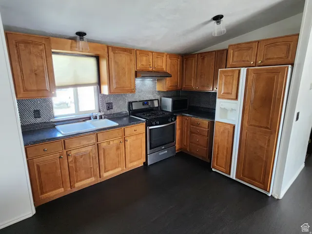 Kitchen featuring wood-finish cabinetry, dark countertops, a stainless steel range, and a dual basin sink